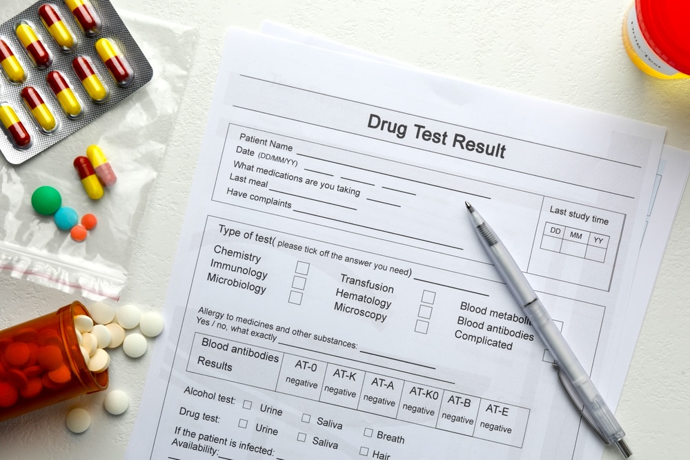 A drug test result form on with a pen and a mix of medicines on the table