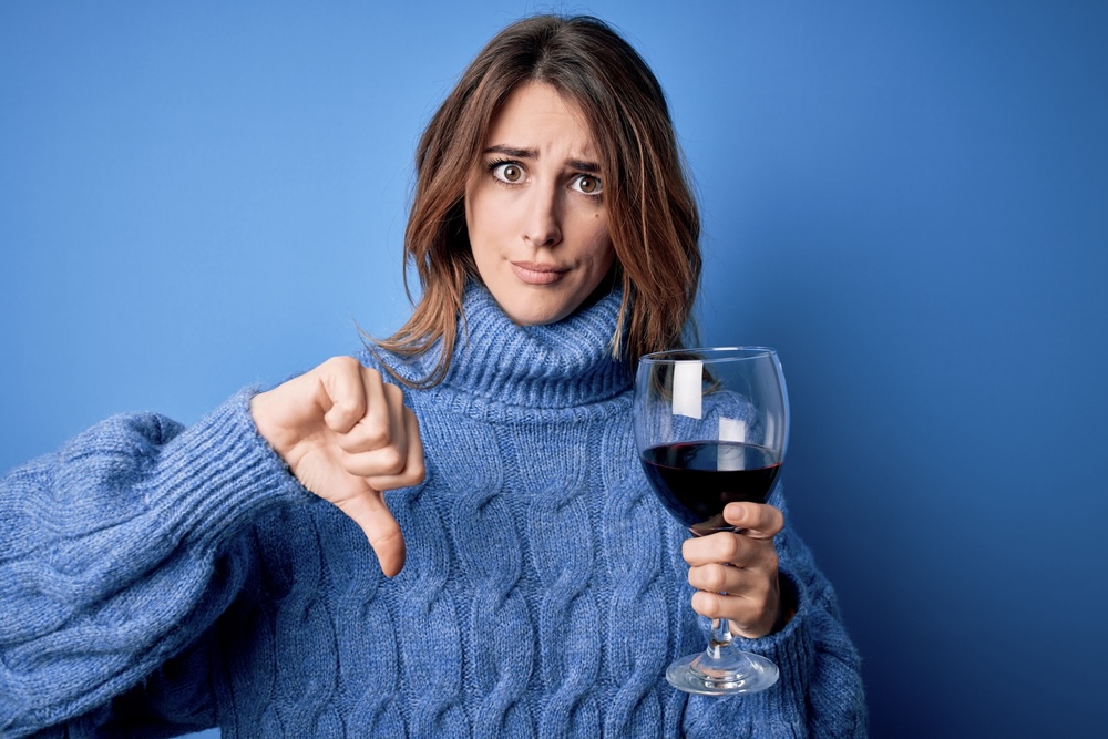 Woman holding a wine glass making a thumbs down sign