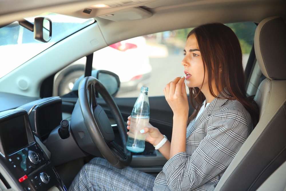 Woman taking a pill and holding bottled water while at the driver’s seat of a car