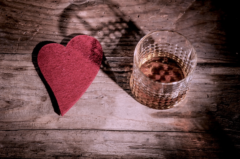 Glass of alcohol on a wooden table with a red heart cutout