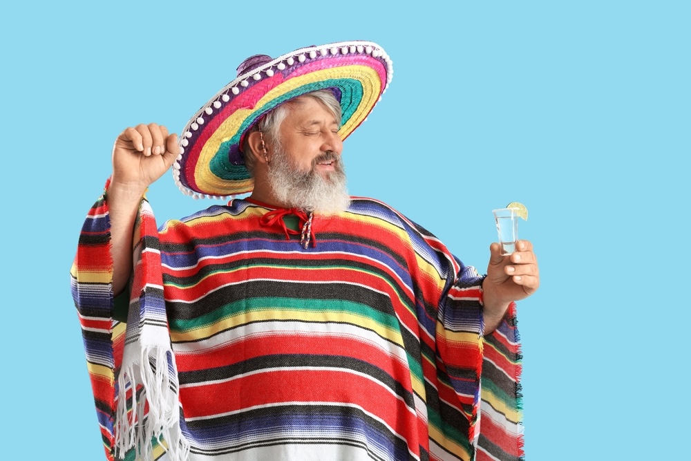 Man in a sombrero and poncho holding a shot of tequila